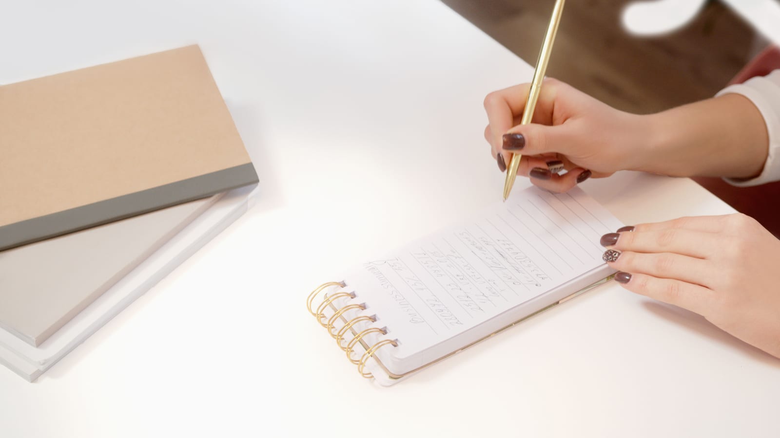 A hand writing notes in a spiral notepad with a pen