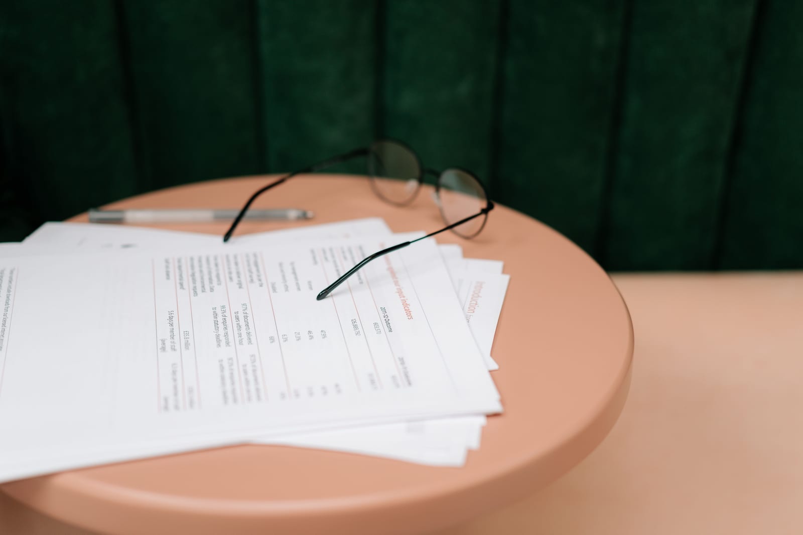 A stack of printed report forms with reading glasses and a pen on a desk