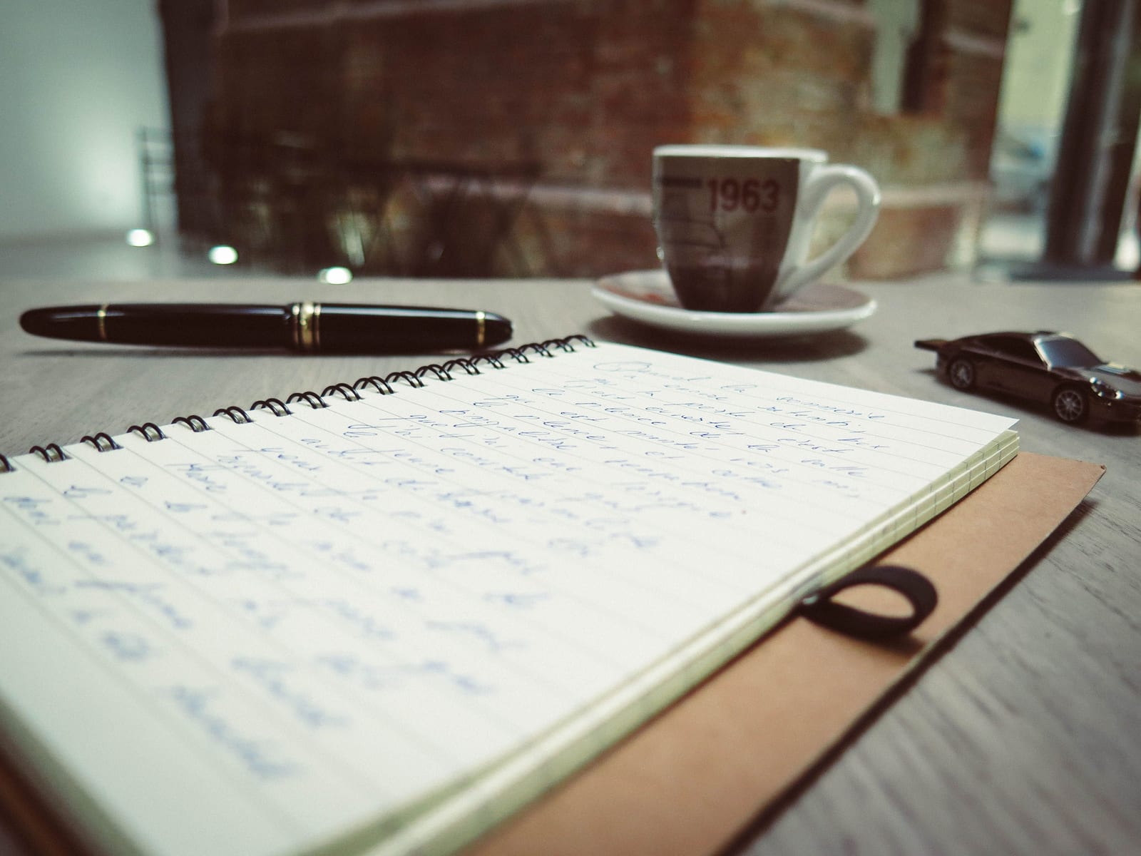 An open notebook filled with handwriting beside a fountain pen on a wooden desk