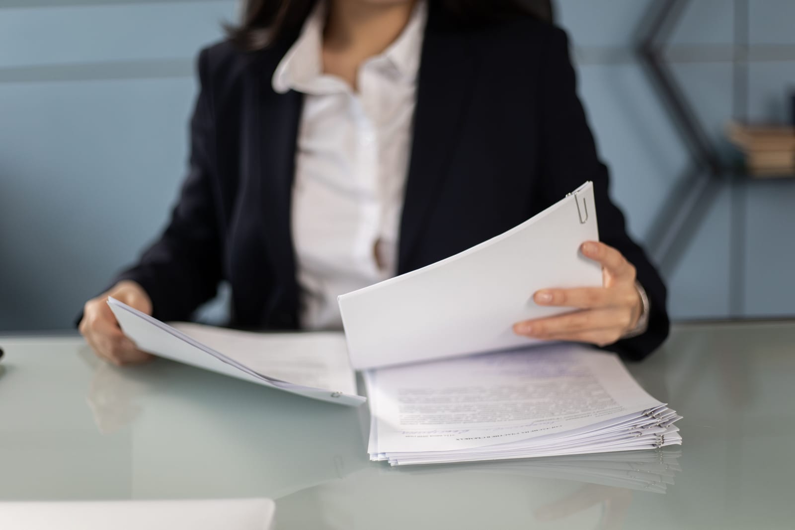 A professional reviewing a thick stack of documents at a glass desk