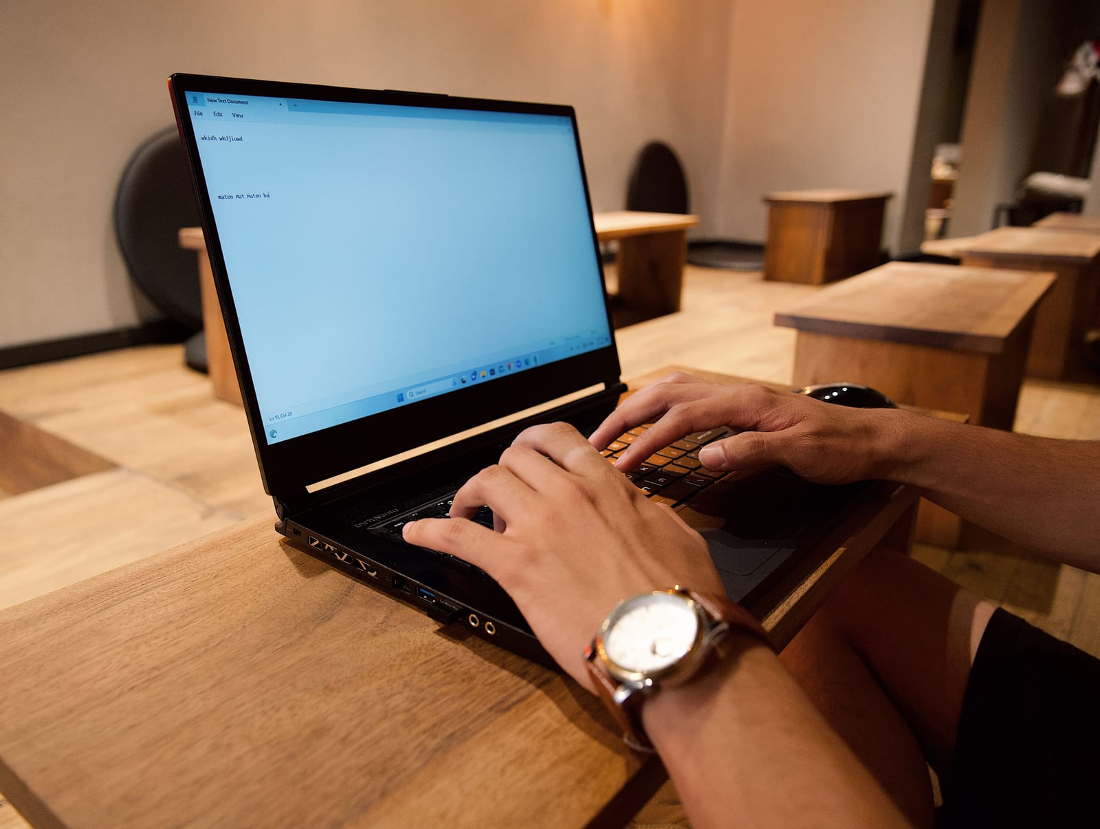 Hands typing on a laptop beside a wristwatch on a wooden table