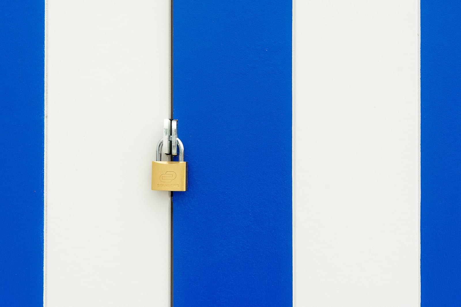 A brass padlock centered on a blue-striped wall