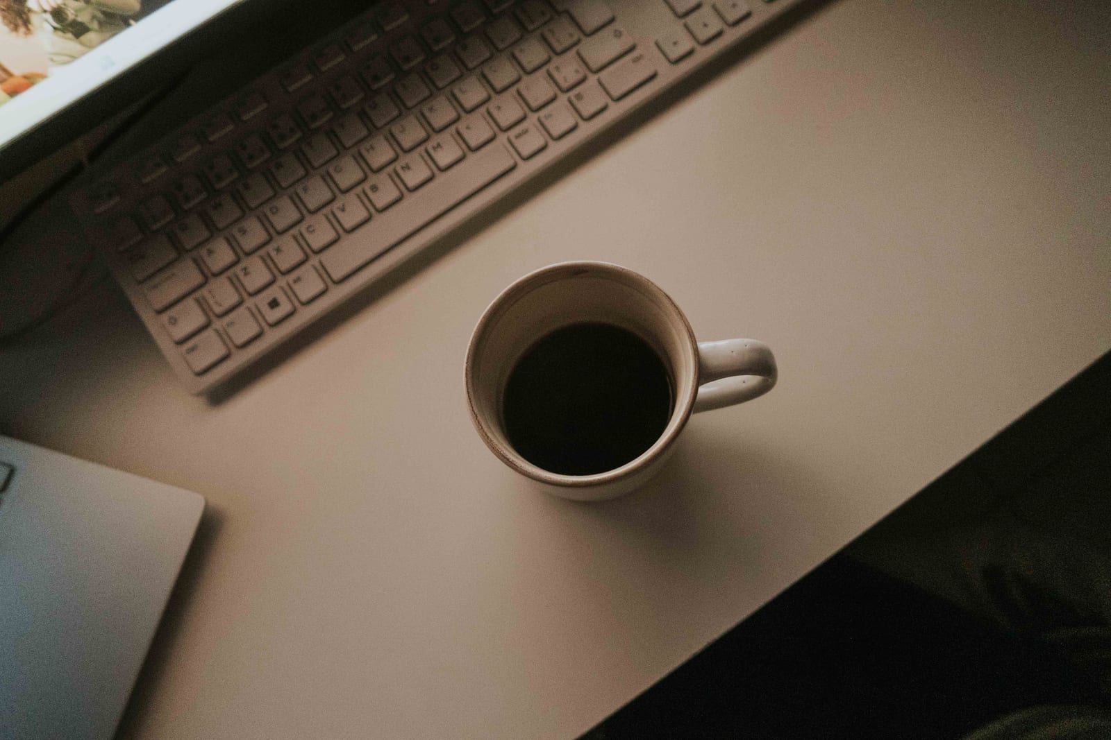A mug of black coffee beside a keyboard on a dimly lit desk