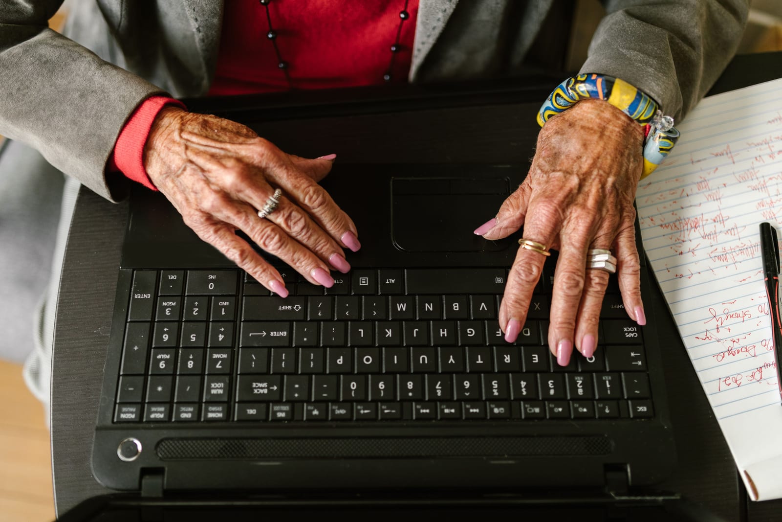 Hands typing on a laptop with handwritten notes beside it on a desk
