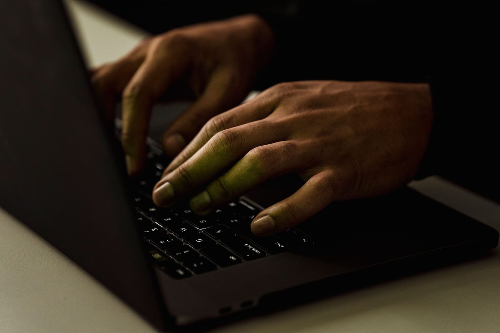 Hands typing on a laptop in low light, the screen glow catching the fingers