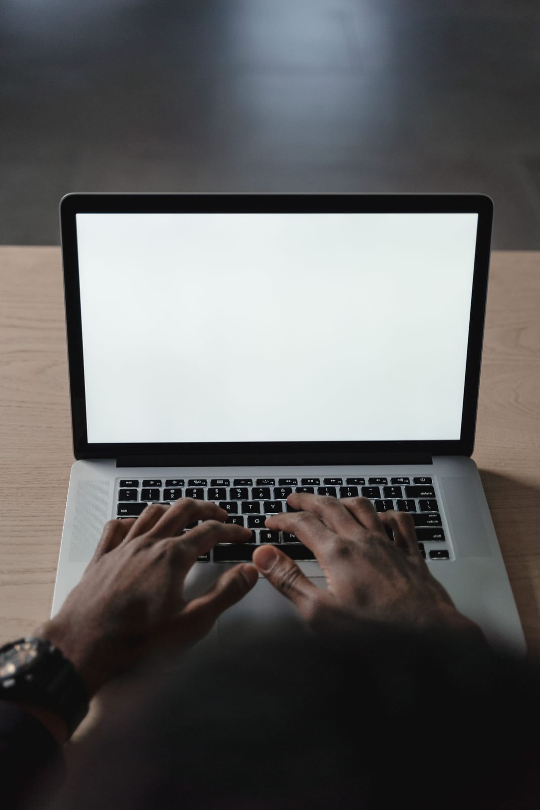 Hands typing on a laptop showing a nearly blank document on a desk